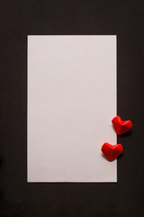 vertical postcard: the white rectangle of paper on a black background and two red hearts. a love letter or greetings with Valentine's day