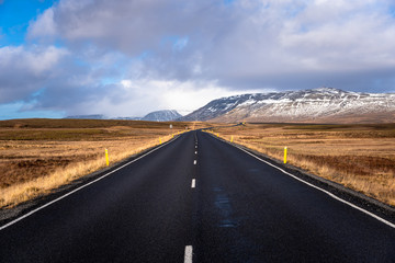 Empty Highway Through a Grassy Plain and Snow-capped Mountains in Iceland in Autumn