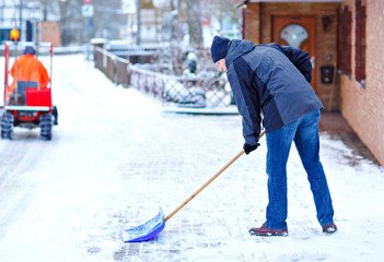 Man with snow shovel cleans sidewalks in winter during snowfall. Winter time in Europe. Young man...