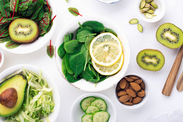 Green ingredients for spring detox salads: spinach, sorrel with red veins, cucumbers, radishes, iceberg lettuce, green peas, avocados, lemon, microgreen, yellow tomatoes on a white background with