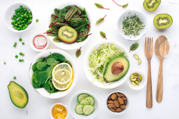 Green ingredients for spring detox salads: spinach, sorrel with red veins, cucumbers, radishes, iceberg lettuce, green peas, avocados, lemon, microgreen, yellow tomatoes on a white background with