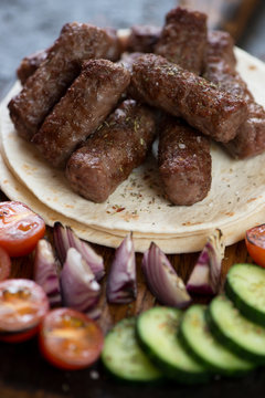 Barbecued balkan cevapi or skinless beef sausages on tortilla flatbread with vegetables, closeup
