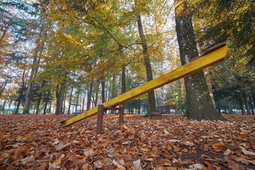 Old yellow seesaw in park viewed from the ground looking up.  Shot in autumn with leaves coverage,...