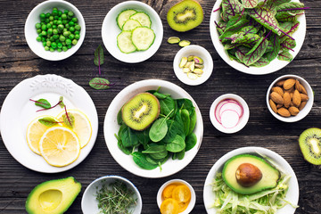 Ingredients for making green salad salads. side dishes, appetizers: sorrel with red veins, spinach, iceberg, pistachios, avocados, cucumbers, radishes, lemon, kiwi, yellow cherry tomatoes on a wooden