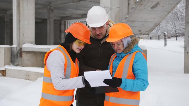 Engineer in hard hat and two women representatives of the customer talking on a snow-covered construction site.