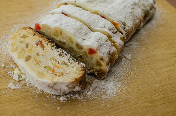 Christmas stollen on darkfestive background with fir twigs, lights and and berries. Close-up on this traditional German dessert
