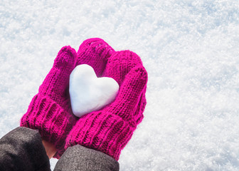 Female hands in knitted mittens with heart of snow in winter day. Love concept. Valentine day background.