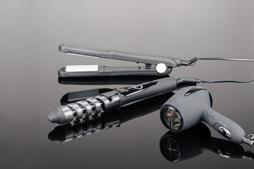 Grey hair iron and grey dryer on the grey mirror background