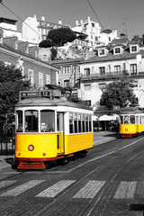 Obrazy  Żółty tramwaj na starych ulicach Lizbony, Alfama, Portugalia, popularna atrakcja turystyczna i miejsce docelowe. Czarno-biały obrazek z kolorowym tramwajem.
