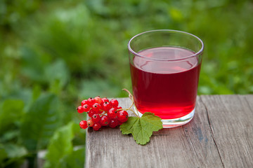 branch of red currant berries and a glass Cup with delicious berry juice on the edge of an old wooden table