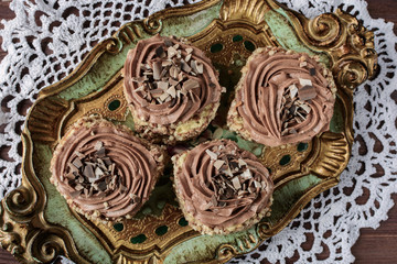 Biscuit cakes sprinkled with nut crumb and decorated with chocolate cream are on a vintage wooden tray on a white lace doily, top view