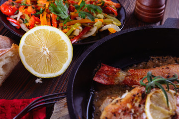Half of lemon next to healthy grilled vegetables  and ocean perches cooked in a cast-iron pan