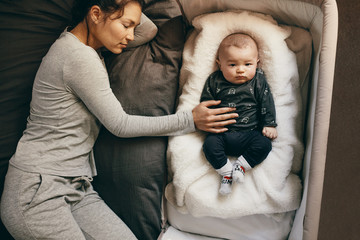 Woman sleeping on bed with her hand on the baby