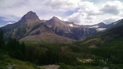 Naklejka na ściany i meble Glacier National Park mountains and forest on a clear day with some clouds. Beautiful