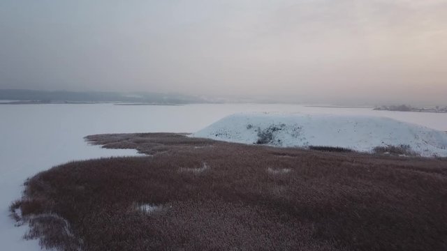 Aerial photography. Winter. Flying over the mound. View of the frozen river and a large hill on the shore.