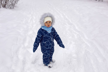 Fototapeta na wymiar baby boy in the winter in blue overalls on the street