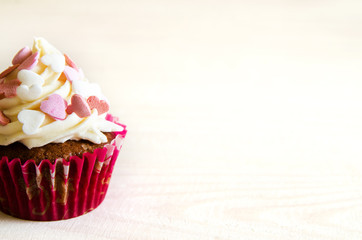 celebratory cupcake for Valentines day and happy birthday on wooden white background with hearts. Give love on a holiday