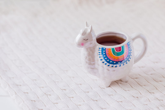 Colorful Llama shaped mug with knitted pullover on the white wooden table