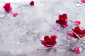 Branches in the snow with red rose buds and hearts on a concrete background with space for text. Valentine's day concept