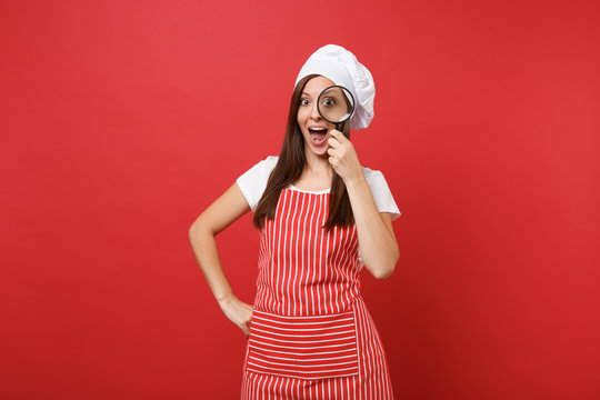 Housewife female chef cook or baker in striped apron white t-shirt toque chefs hat isolated on red wall background. Housekeeper woman hold and look through magnifying glass. Mock up copy space concept - Powered by Adobe