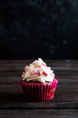 celebratory cupcake for Valentines day and happy birthday on wooden black background with hearts. Give love on a holiday