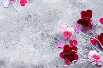 Branches in the snow with pink and red rose buds and hearts on a concrete background with space for text. Valentine's day concept