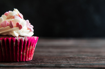 celebratory cupcake for Valentines day and happy birthday on wooden black background with hearts. Give love on a holiday