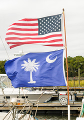 USA Flag and South Carolina State Flag fly together, unfurled, on the same flagpole in the wind at a Hilton Head Island Dock, USA.
