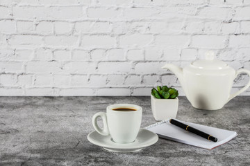 White cup with black coffee and a blank notepad, pen on a gray stone background. Place for text.