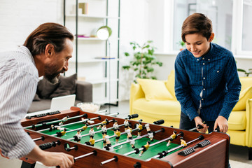 Emotional boy and his father playing table football at home
