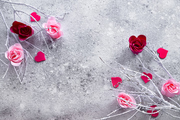 Branches in the snow with pink and red rose buds and hearts on a concrete background with space for text. Valentine's day concept