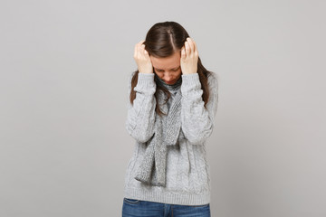 Tired young woman in gray sweater, scarf putting hands on lowered head isolated on grey background in studio. Healthy fashion lifestyle people sincere emotions cold season concept. Mock up copy space.