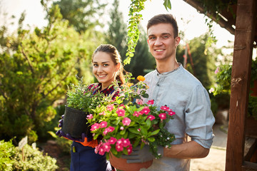 Gardeners happy boy and girl hold pots with plants in beautiful gardens on a warm sunny day