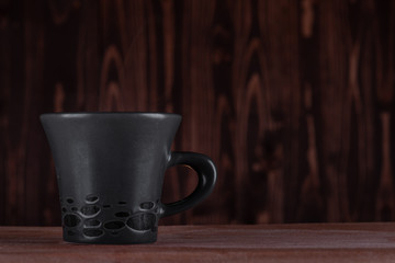 a dark gray cup on a wooden surface and a background