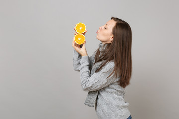 Side view of young woman in sweater, scarf blowing sending air kiss to oranges isolated on grey background. Healthy fashion lifestyle, people sincere emotions, cold season concept. Mock up copy space.