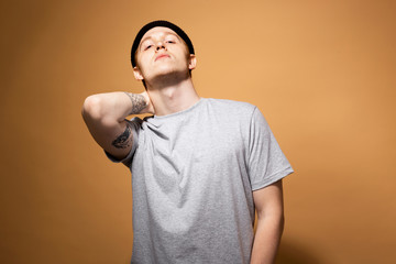 Young stylish guy dressed in a gray shirt and black hat with tattoo on his hand is posing on the...