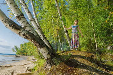 A woman in a bright outfit, in a colorful skirt joyful among the birches on the river Bank, the sea.