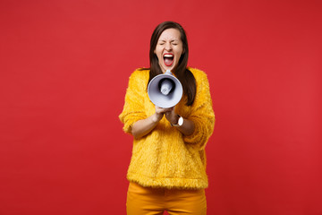 Crazy young woman in yellow fur sweater keeping eyes closed, screaming on megaphone isolated on...