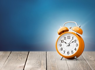 Orange retro alarm clock on wooden table on wall background