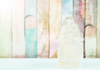 Using crystal Selenite tower for loading rose quartz pendulum, light blue table and pastel color wooden board background. Divination and fortune telling concept.