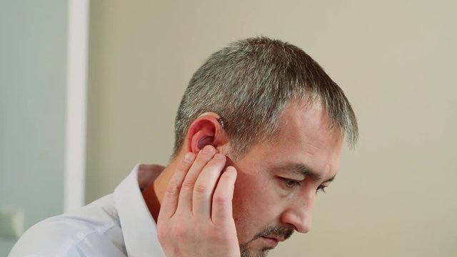 A middle aged man tries on a hearing aid.