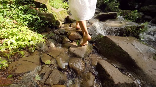 Young Attractive Woman in White Dress Walking Barefoot on a Path to Small Waterfall in Tropical Rainforest Jungle. Carefree Lifestyle Travel 4K Slowmotion Footage. Bali, Indonesia.