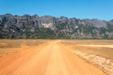 Red clay dirt road in Laos leading to mountains