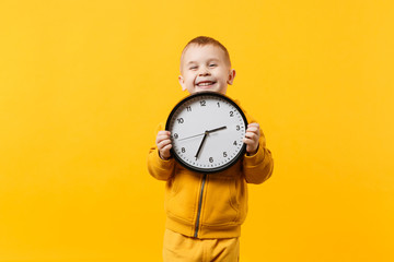 Little kid boy 3-4 years old wearing yellow clothes hold clock isolated on orange wall background,...