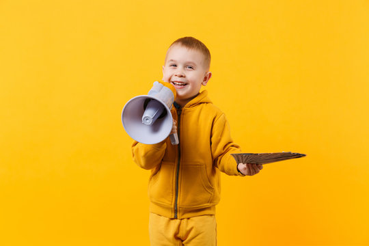 Little happy kid boy in yellow clothes hold fan of money in dollar banknotes, megaphone isolated on orange wall background, children studio portrait. Childhood lifestyle concept. Mock up copy space.