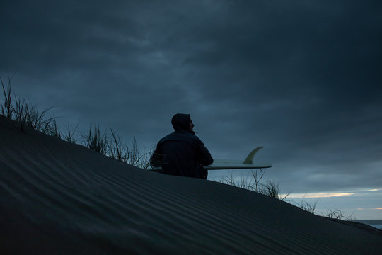 Man with surfboard sitting on seashore
