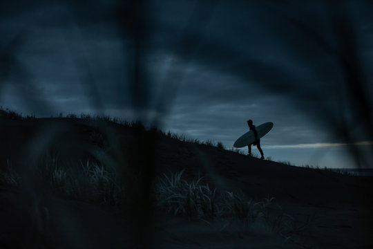 Silhouette of man carrying surfboard while walking on seashore