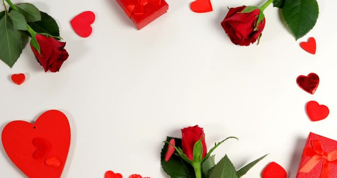 Red roses, gift boxes and heart shape of confetti on white surface in circle formation 4k