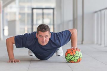 Sporty man doing push ups with football ball