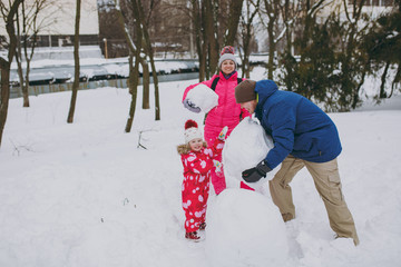 Fototapeta na wymiar Happy family woman, man little girl in winter warm clothes playing, making snowman in snowy park or forest outdoors. Winter fun, leisure on holidays. Love relationship family people lifestyle concept.